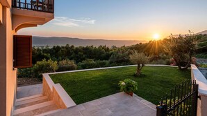 A residential property with a balcony, a well-maintained lawn, and a view of the sunset over the hills. - Spacious Apartment, Private Terrace in the Countryside, Wi-fi and Parking (Konavle)