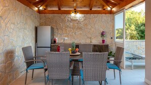 A stone-walled kitchen with a stone countertop, a refrigerator, and a sink. There are wicker chairs with blue cushions around a table with a fruit bowl and a vase. - Spacious Apartment, Private Terrace in the Countryside, Wi-fi and Parking (Konavle)