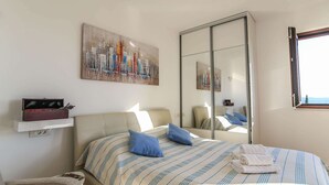 A bedroom with a bed, pillows, a bedside table, a mirror, and artwork on the wall. - Spacious Apartment, Private Terrace in the Countryside, Wi-fi and Parking (Konavle)