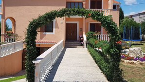 A two-story house with a tiled roof, a balcony with a white railing, and a garden with colorful flowers. - Apartment in Vrsi Near the Sea (Vrsi)