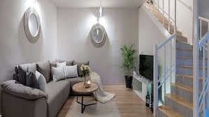 A modern living room with a grey sofa, two wall-mounted mirrors, a round coffee table with a candle, and a staircase with wooden steps and blue railings. - Luxury Villa Lelu With Heated Saltwater Pool, Parking, High Speed Internet, Bbq, el. car Charge T2 (Split)