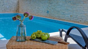 A poolside setting with a wicker table holding a vase with flowers, a bunch of grapes, and a few apples. - Luxury Villa Lelu With Heated Saltwater Pool, Parking, High Speed Internet, Bbq, el. car Charge T2 (Split)