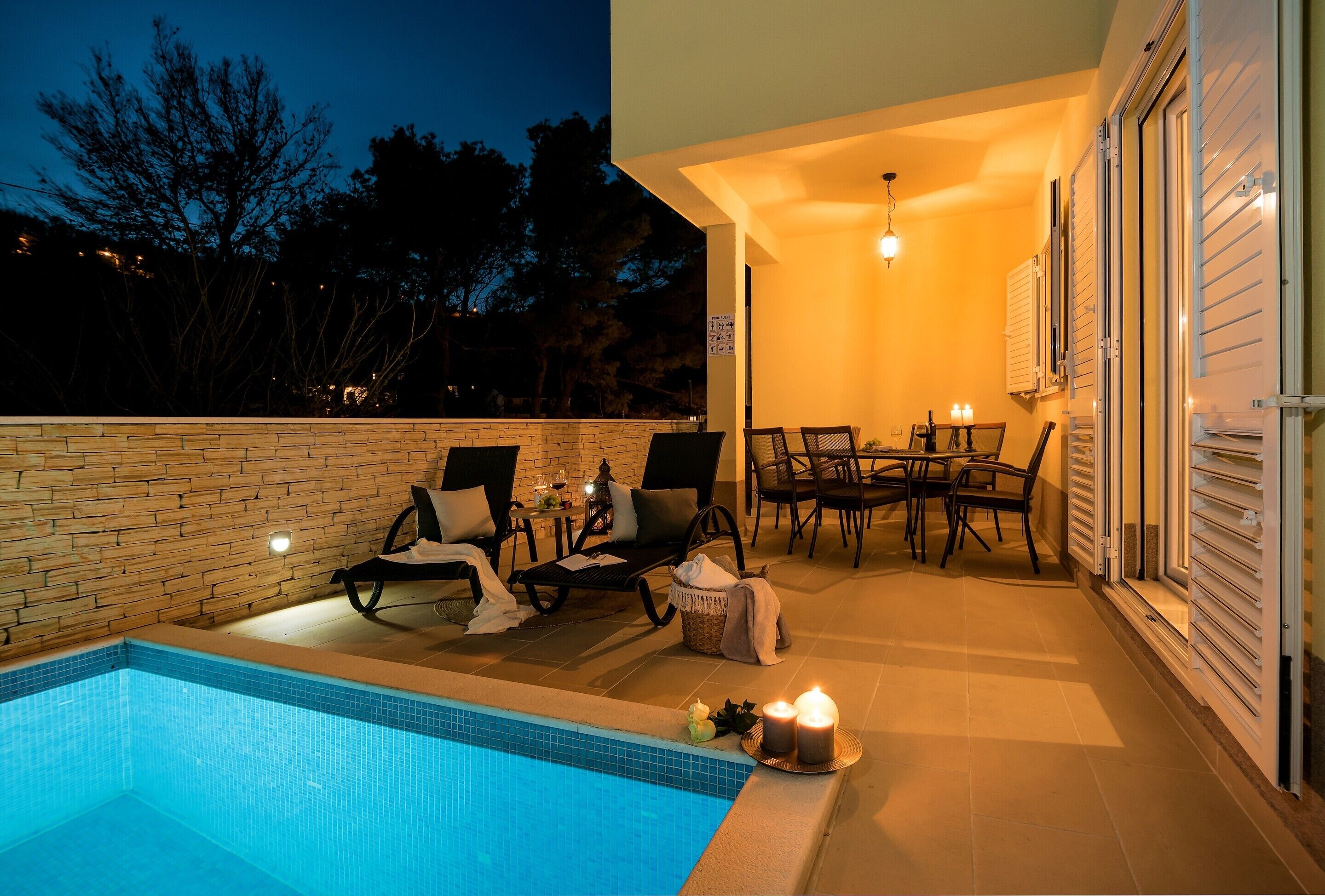 A poolside area with a tiled pool, lounge chairs, a table with chairs, and candles.