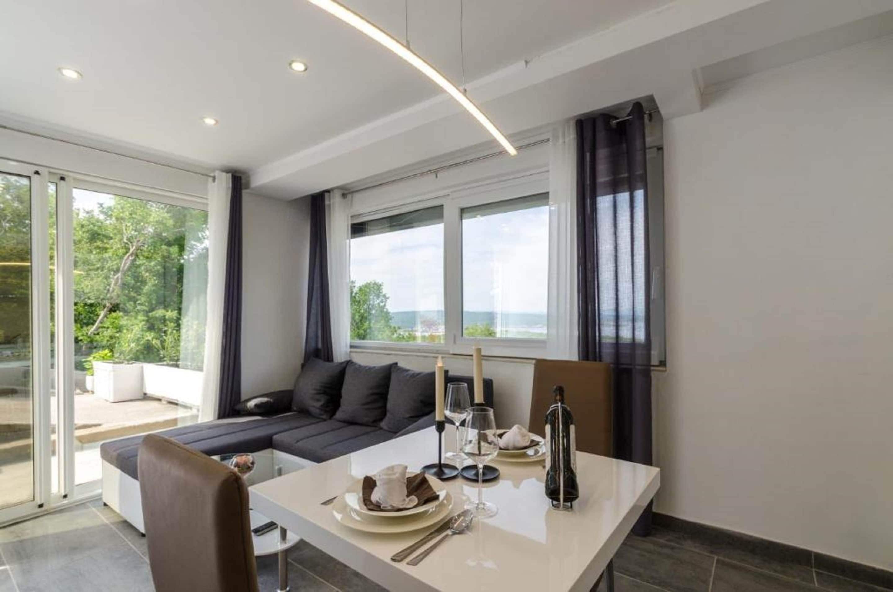 Et moderne spiseområde med et bord dækket til to personer, en sofa og et stort vindue med udsigt.