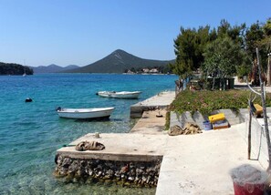 Une zone côtière où des bateaux sont amarrés à un quai, avec une eau claire et une chaîne de montagnes en arrière-plan.