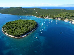 An aerial view of a coastal area with a small island surrounded by clear blue waters, numerous boats, and a backdrop of green hills. - Apartment in Molat With sea View (Zadar)