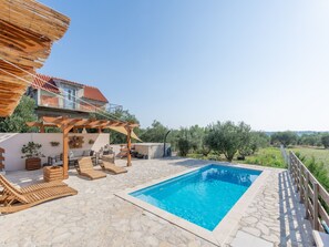 Ein Poolbereich mit einer Steinterrasse, Holzliegen und einer Pergola.