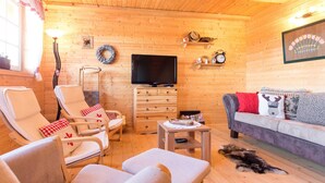 A cozy cabin interior with wooden walls, a television, a sofa, and two lounge chairs. - Holiday Home Ravna Gora Near Risnjak Park (Ravna Gora)