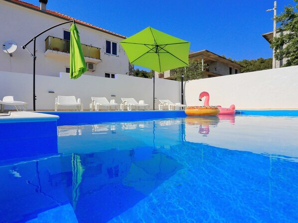 A swimming pool with clear blue water, surrounded by white lounge chairs and a green umbrella. - Modern Apartment in Bibinje With Pool (Bibinje)