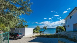 A residential area with a gravel driveway, a parked car, a white building, and a view of the sea. - Maslenica Pool Villa With Charm (Jasenice)