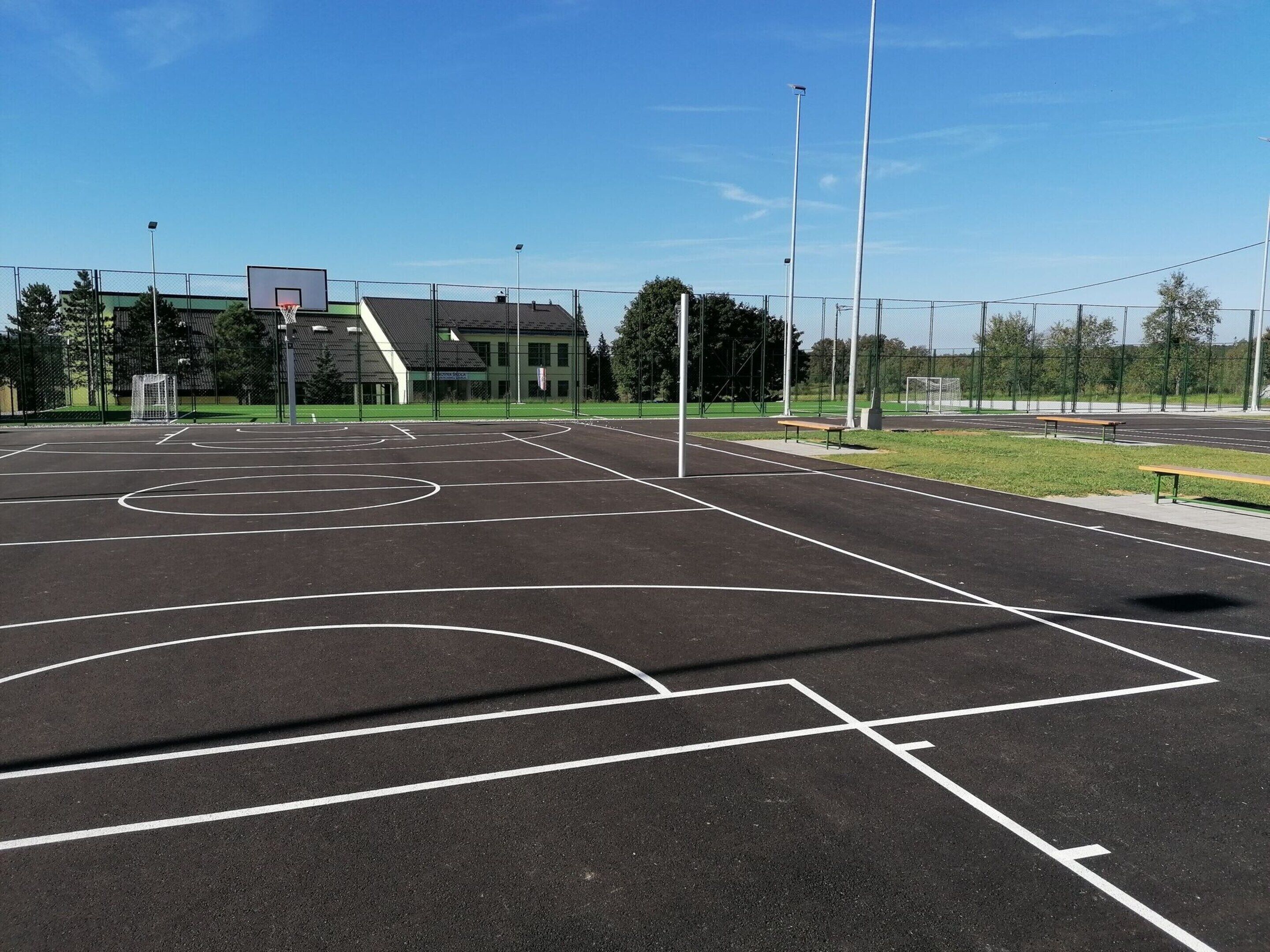A basketball court with a goal post, surrounded by a fence, and a building in the background.