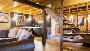 Un salon chaleureux avec un canapé, des poutres en bois et une cuisine en arrière-plan.