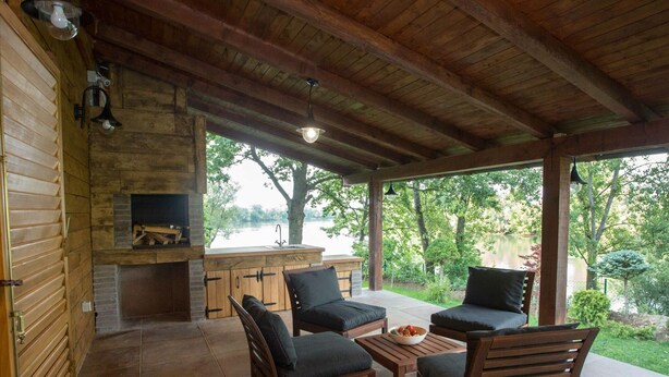 Un patio couvert aménagé avec du mobilier en bois, une cheminée en pierre et une vue sur un lac.