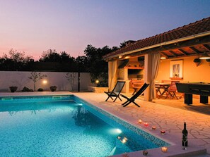 Une piscine avec des chaises longues, un espace barbecue et une bouteille de vin sur la terrasse.