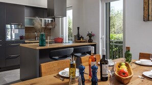 A modern kitchen with a central island, dark cabinetry, and a dining area with a wooden table set for two. - Modern Countryside Villa Near the Sea, Private Swimming Pool, Lovely Guesthouse (Polaca)