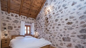 A bedroom with a stone wall, wooden ceiling, a wooden bed, a nightstand, a lamp, and a window with curtains. - Seaside Retreat in Marina di Grosseto (Starigrad)
