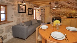 A cozy room with a grey sofa, wooden dining table set for four, and a kitchen area with a brick wall and wooden beams. - Seaside Retreat in Marina di Grosseto (Starigrad)