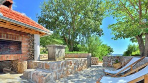 An outdoor patio with stone flooring, a brick fireplace, and a lounge chair. - Seaside Retreat in Marina di Grosseto (Starigrad)