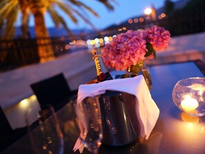 A table with a champagne bottle, a vase of pink flowers, and a lit candle. - Villa on an Exclusive Location in Dubrovnik With Pool (Dubrovnik)