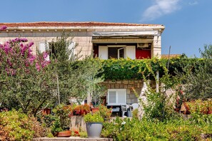 A two-story building with a tiled roof, a balcony with a white railing, and a garden with various plants and flowers.