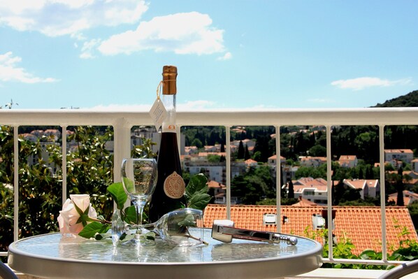 A table with a bottle, a wine glass, a flower, and a candle on a balcony overlooking a cityscape.