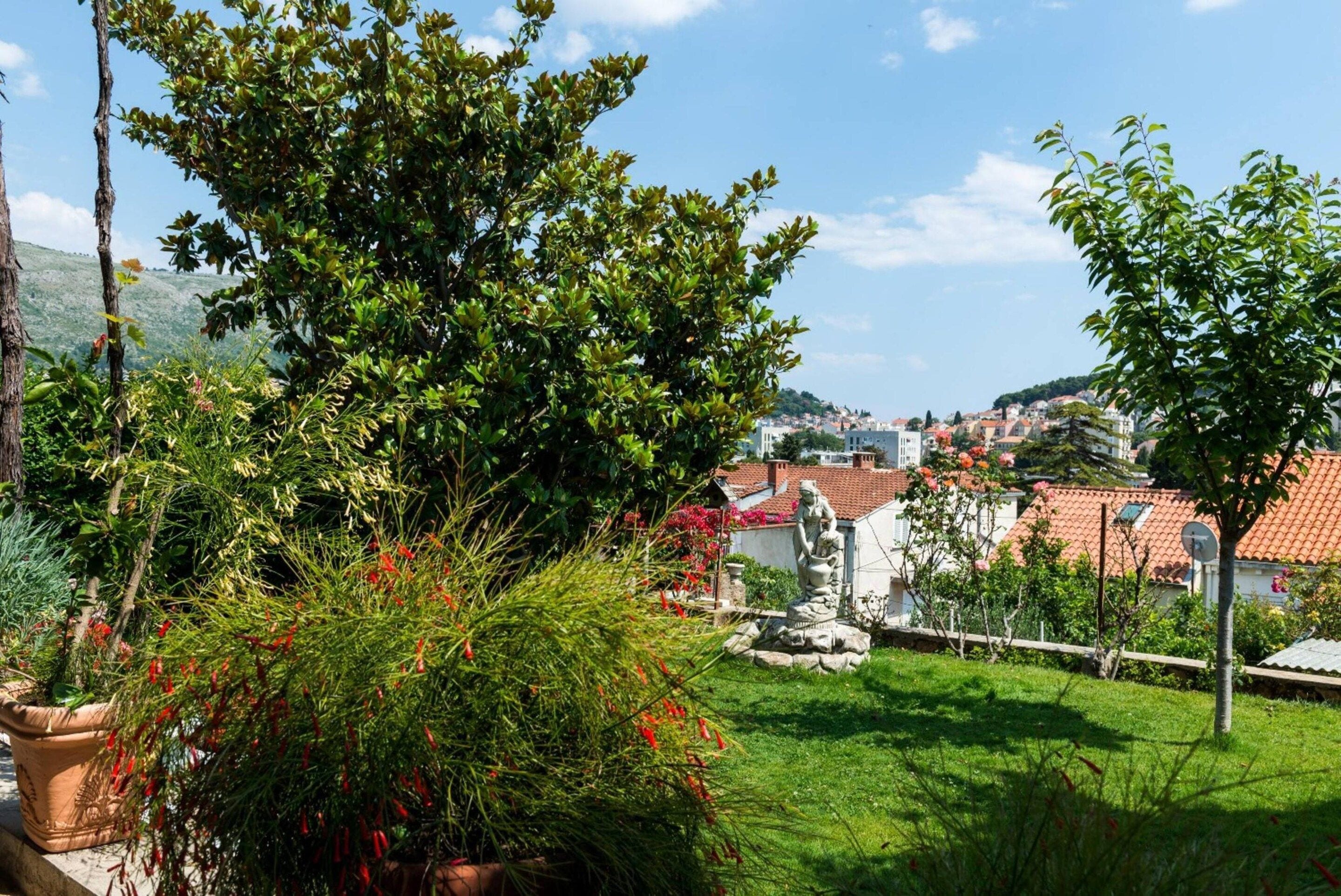 A residential area with a view of a town, a grassy lawn, and a statue.