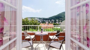 A balcony with a table and chairs, a bottle, and a view of a town and hills. - Dubrovnik Apartment With Private Terrace (Dubrovnik)