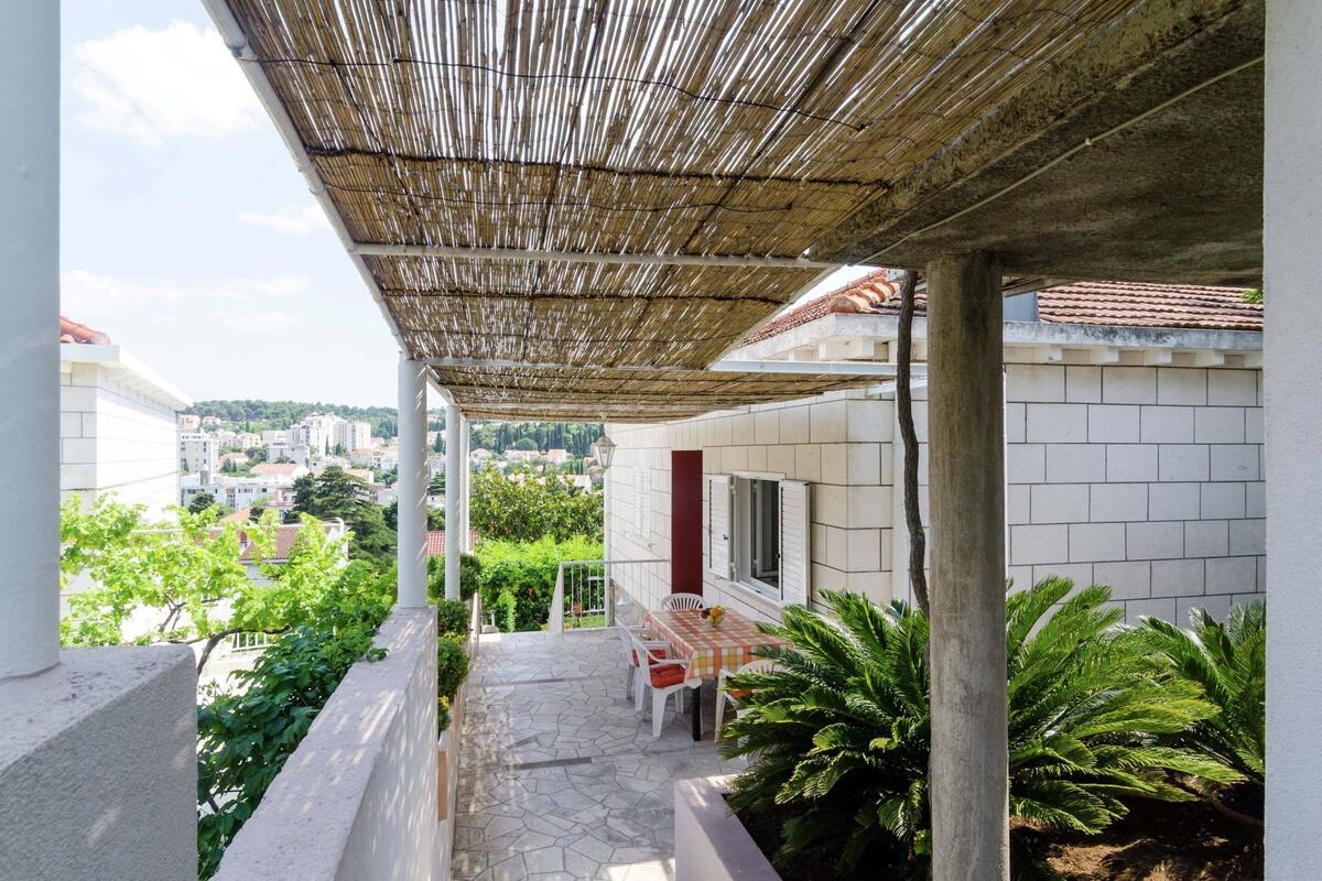 A covered outdoor area with a stone floor, a table with chairs, and a view of a cityscape.