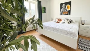 A bedroom with a bed, a bedside table, a lamp, a window with curtains, and a plant. - Dubrovnik Apartment With Private Terrace (Dubrovnik)