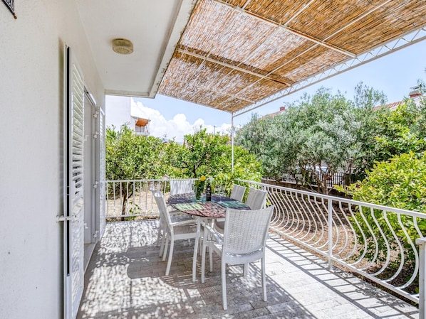 A covered outdoor patio with a table and chairs, surrounded by a white metal fence and greenery.