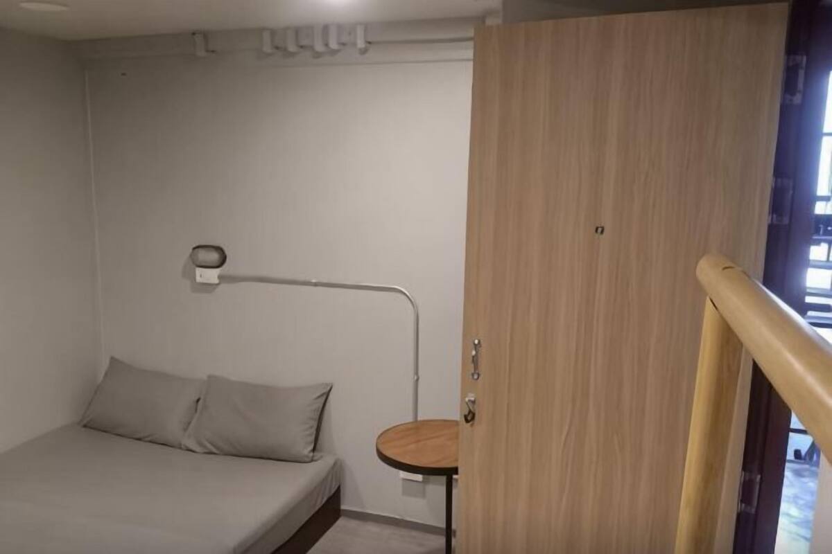 A bedroom with a bed, a bedside table, a lamp, and a wooden door.
