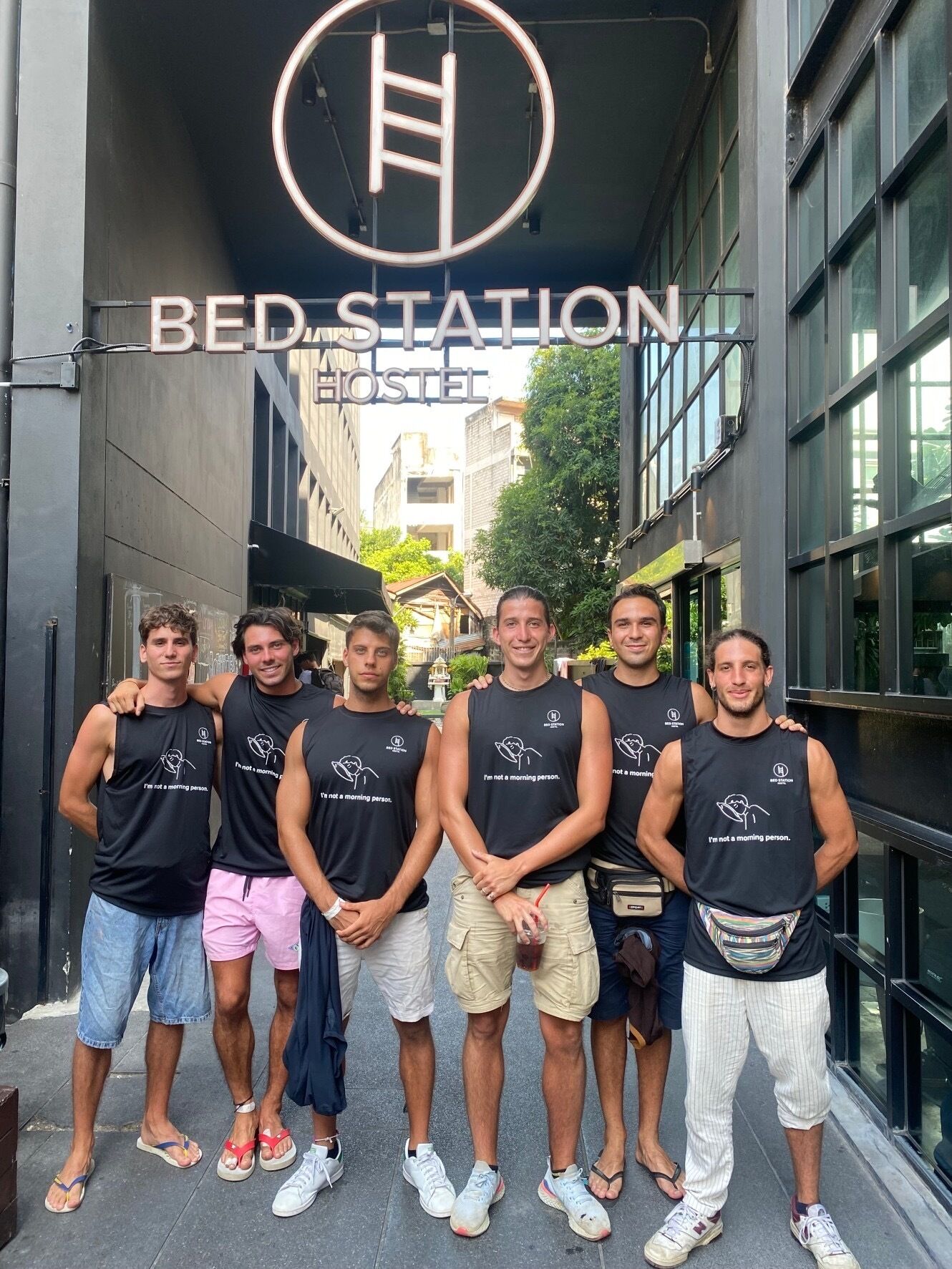 Un grupo de personas frente a un edificio con un cartel que dice "BED STATION HOSTEL".