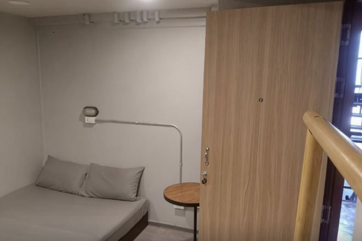 A bedroom with a bed, a bedside table, a lamp, and a wooden door.