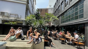 An outdoor seating area with concrete steps and tables, surrounded by buildings with large windows and air conditioning units. - BED STATION HOSTEL KHAOSAN (Bangkok)