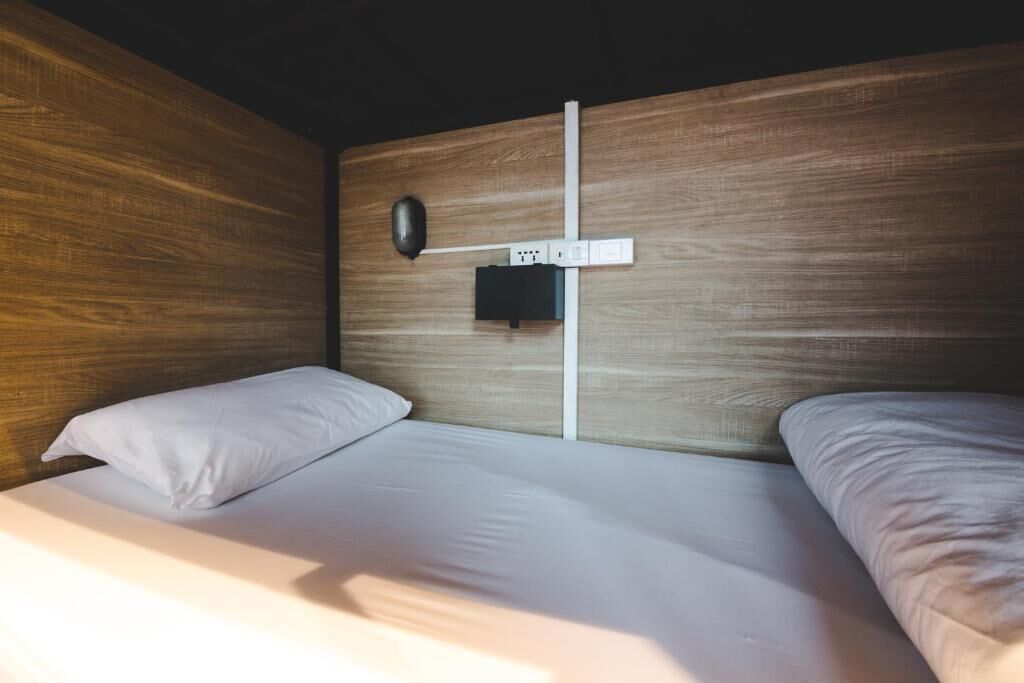 Une chambre avec une tête de lit en bois, une lampe fixée au mur et une prise de courant.