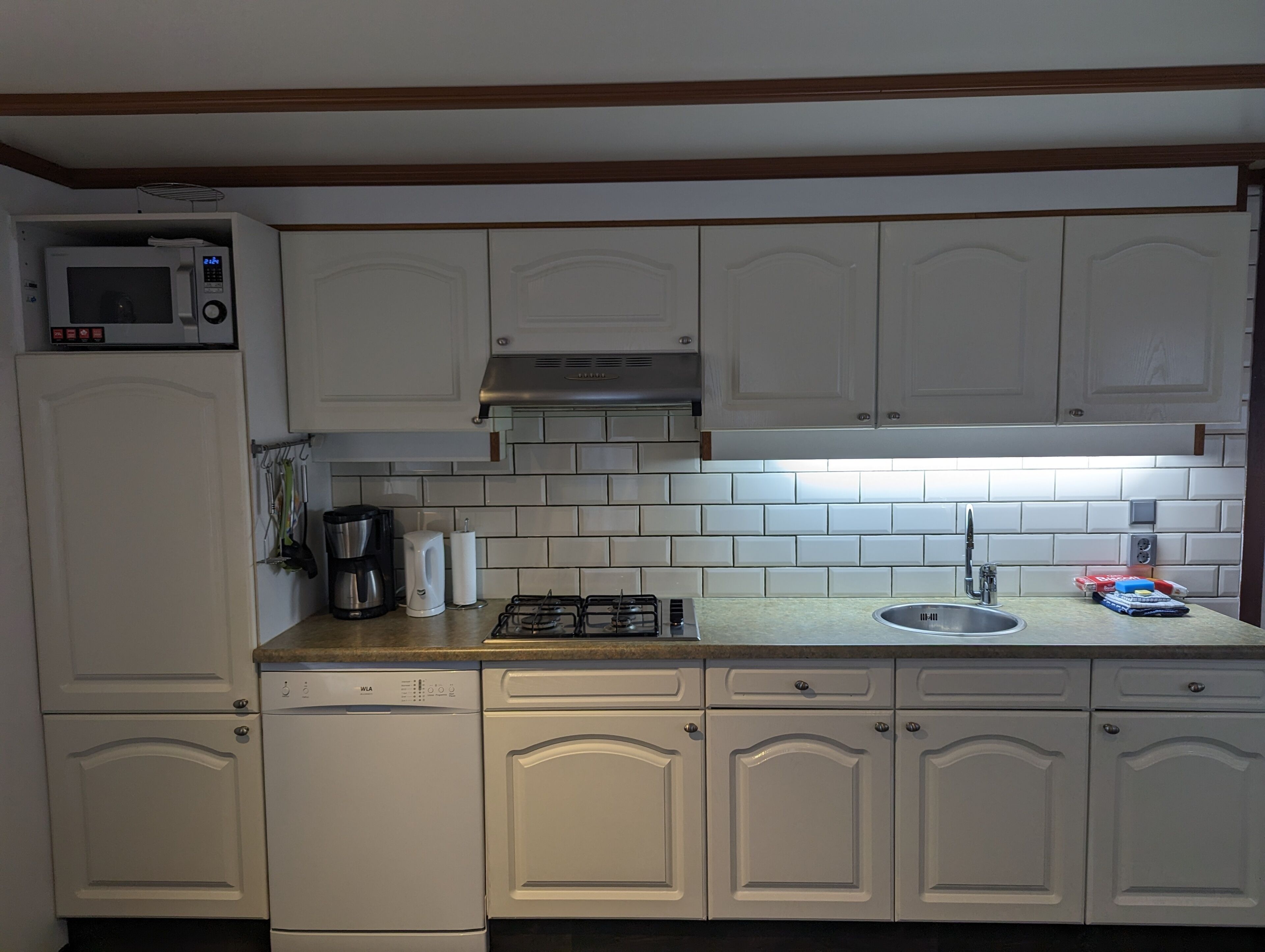 Cocina compacta con armarios blancos, microondas, estufa a gas y pileta.