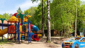 A playground with a slide and climbing structures, surrounded by trees.