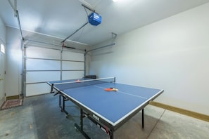Una mesa de ping pong en una habitación con una puerta de garaje y un proyector instalado en el techo.