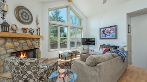 A cozy living room with a stone fireplace, a large window, a comfortable sofa, and a television. - Blue Ridge Daze ~ Mtn Vista, Fireplace, Fire Pit, Pet Friendly, 30 mins to AVL. (Burnsville)