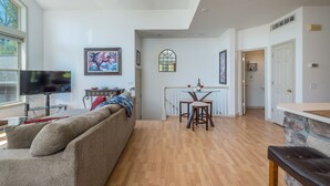A living room with a sofa, a TV, a dining area with a table and chairs, and a kitchen area with a stone countertop. - Blue Ridge Daze ~ Mtn Vista, Fireplace, Fire Pit, Pet Friendly, 30 mins to AVL. (Burnsville)