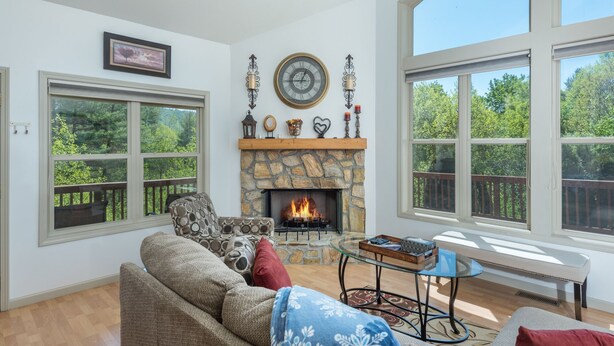 A cozy living room with a stone fireplace, large windows, and a comfortable seating area. - Blue Ridge Daze ~ Mtn Vista, Fireplace, Fire Pit, Pet Friendly, 30 mins to AVL. (Burnsville)