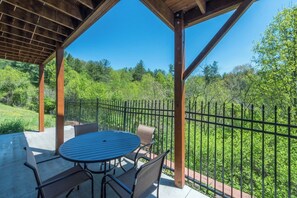A covered outdoor seating area with a table and chairs, surrounded by a metal fence, overlooking a lush green landscape. - Blue Ridge Daze | Fireplace~Pet Friendly~Near Town (Burnsville)