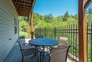 A covered patio with a round table and four chairs, surrounded by a black metal fence. - Blue Ridge Daze | Fireplace~Pet Friendly~Near Town (Burnsville)