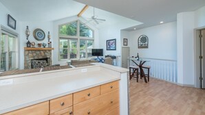 A spacious living area with a stone fireplace, large windows, a ceiling fan, and a dining table with chairs. - Blue Ridge Daze ~ Mtn Vista, Fireplace, Fire Pit, Pet Friendly, 30 mins to AVL. (Burnsville)