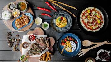 Variedad de platos, incluyendo carne a la parrilla, arroz y una pizza, dispuestos sobre una mesa de madera.