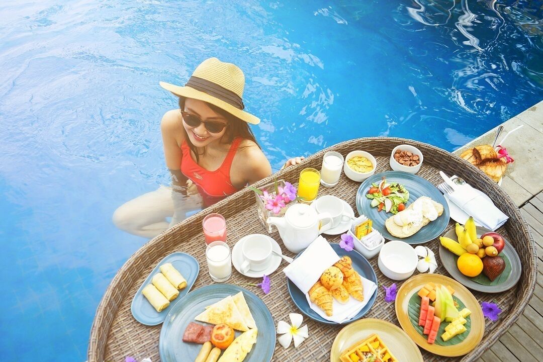 A dining setup by a pool with various breakfast items including fruits, pastries, and beverages.