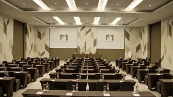 Un salón de conferencias con filas de mesas, sillas y pantallas de presentación.