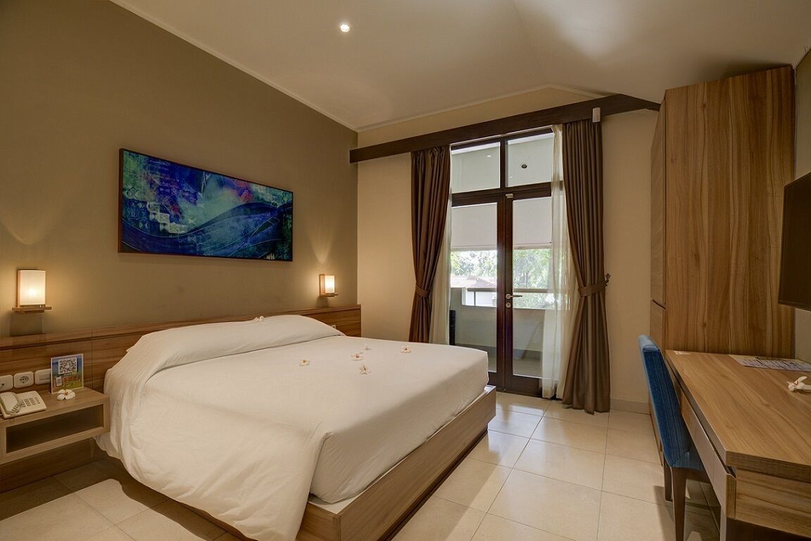 A hotel room with a large bed, a desk, a chair, a painting on the wall, and a view through the window.
