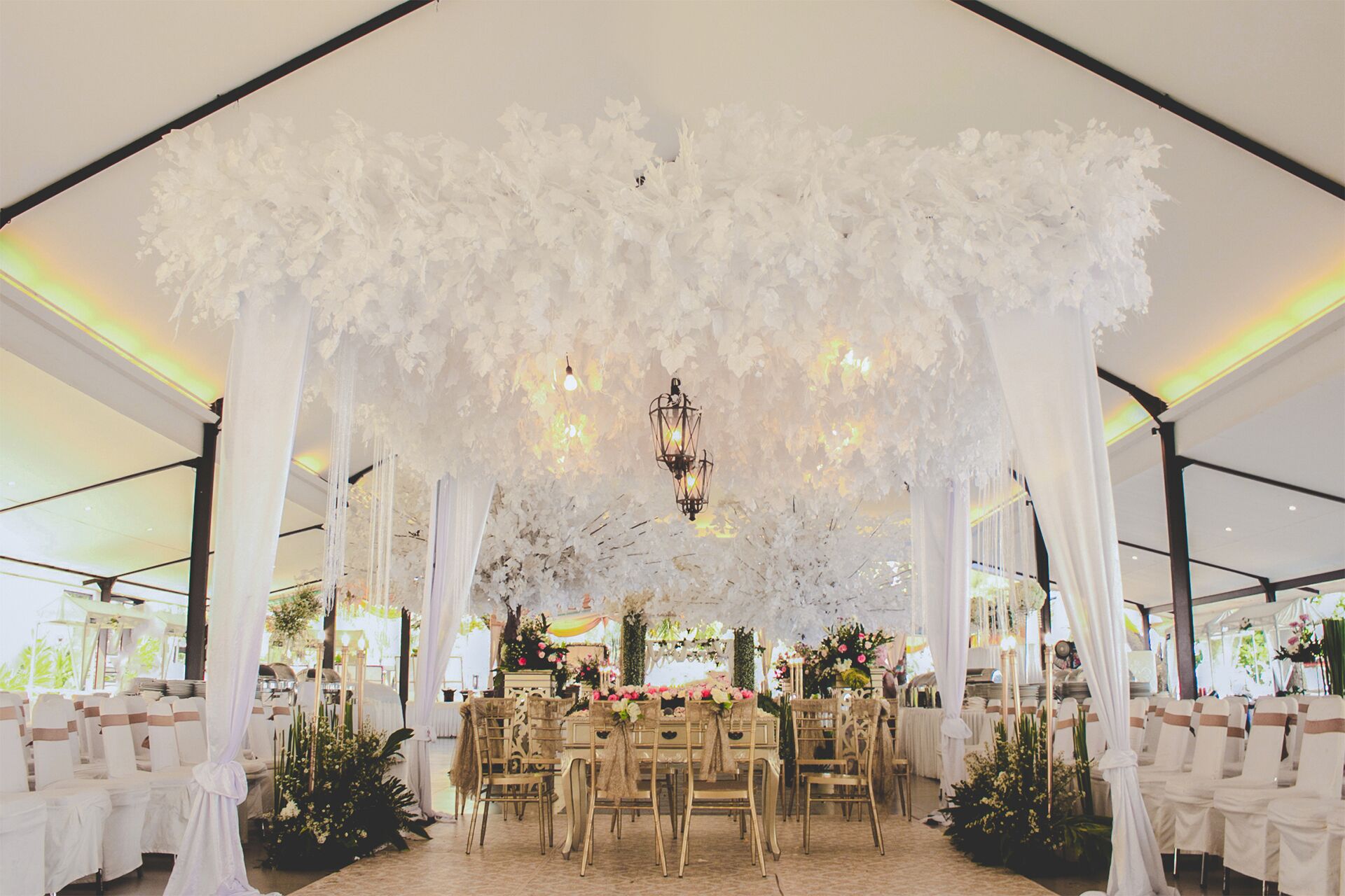 A tented wedding venue with white drapery, chandeliers, and floral arrangements.