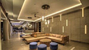A modern lobby with a sectional sofa, round ottomans, and pendant lighting. - Mambruk Hotel & Convention (Anyer)